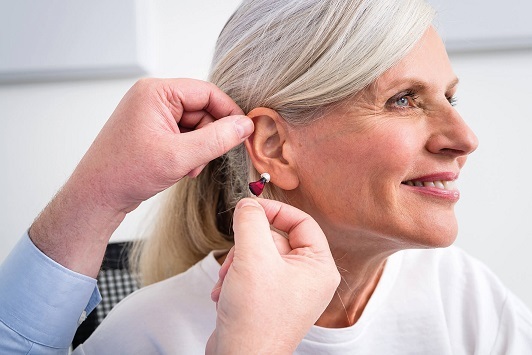 Eine Seniorin bekommt ein modernes Hörgerät ins Ohr eingesetzt und lächelt zufrieden.